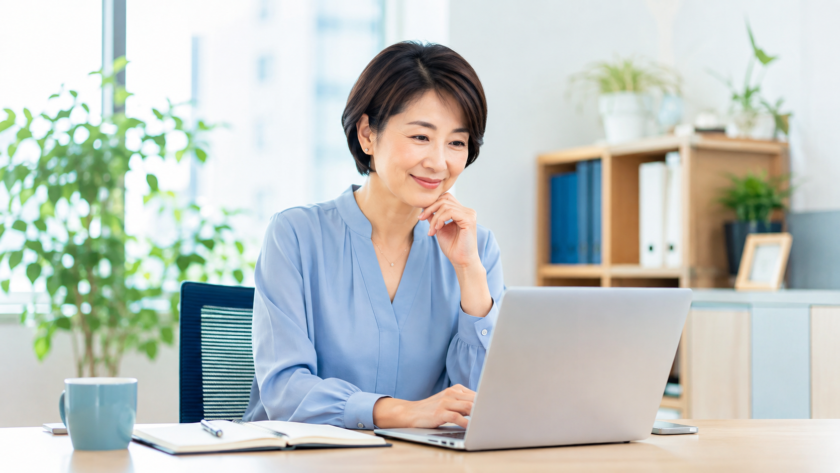明るいオフィスでノートパソコンを使い、落ち着いて仕事を進める40代女性管理職